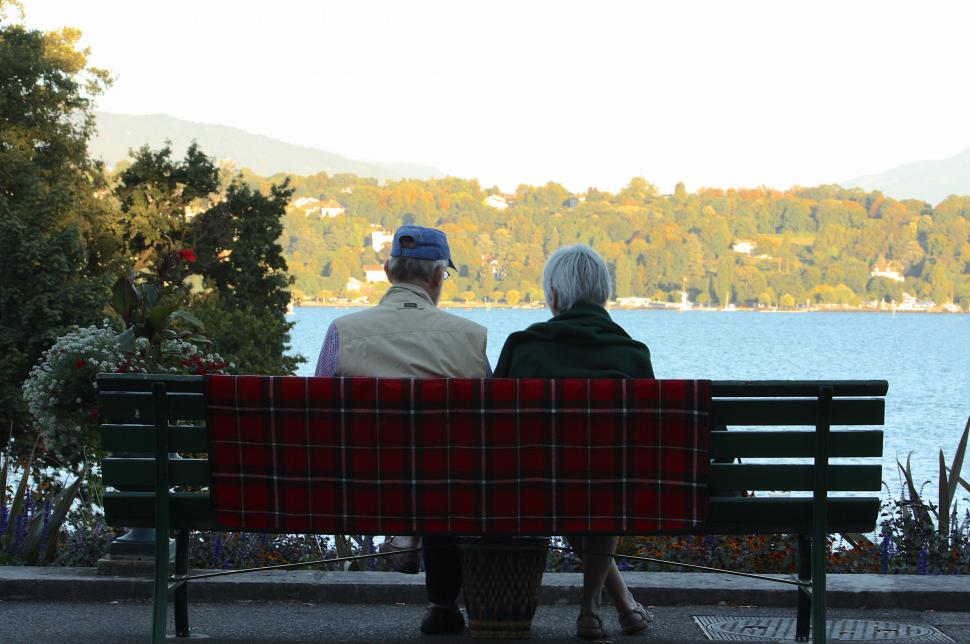 Casal de velhos, sentados a contemplar a paisagem de um lago, simbolizando o envelhecer juntos - amor