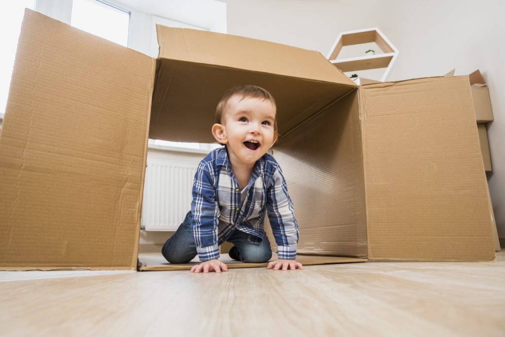 menino brincando sob uma caixa de papelão, representando forma de brincadeira criativa, que favorece a educação infantil.